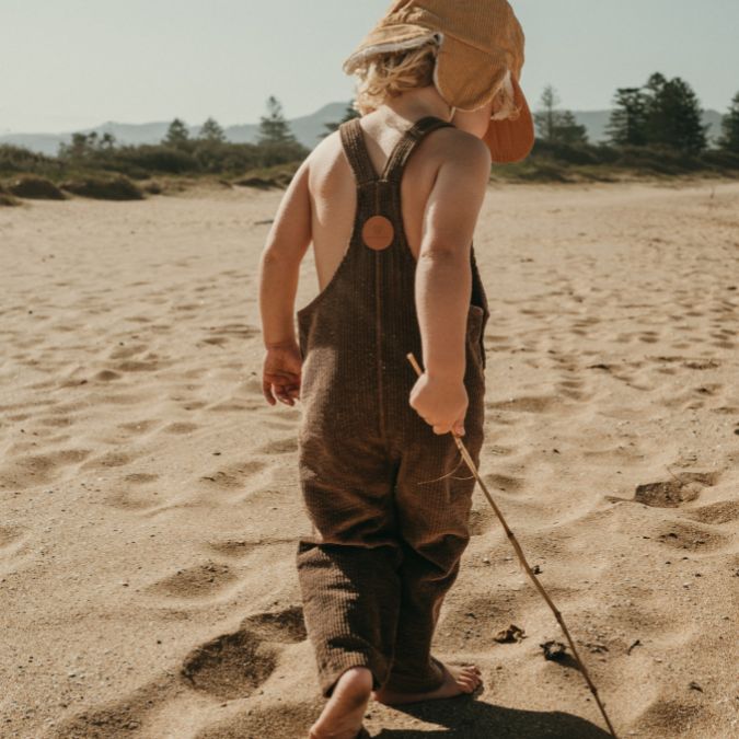boy walking on sand in his brown Kids and toddlers corduroy overalls or dungarees
