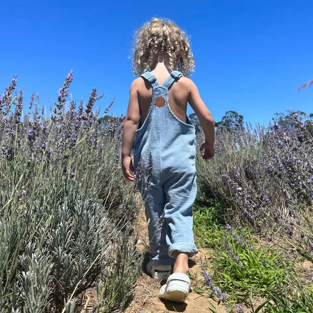 girl wearing her Kids and toddlers blue corduroy overalls or dungarees in a field of flowers