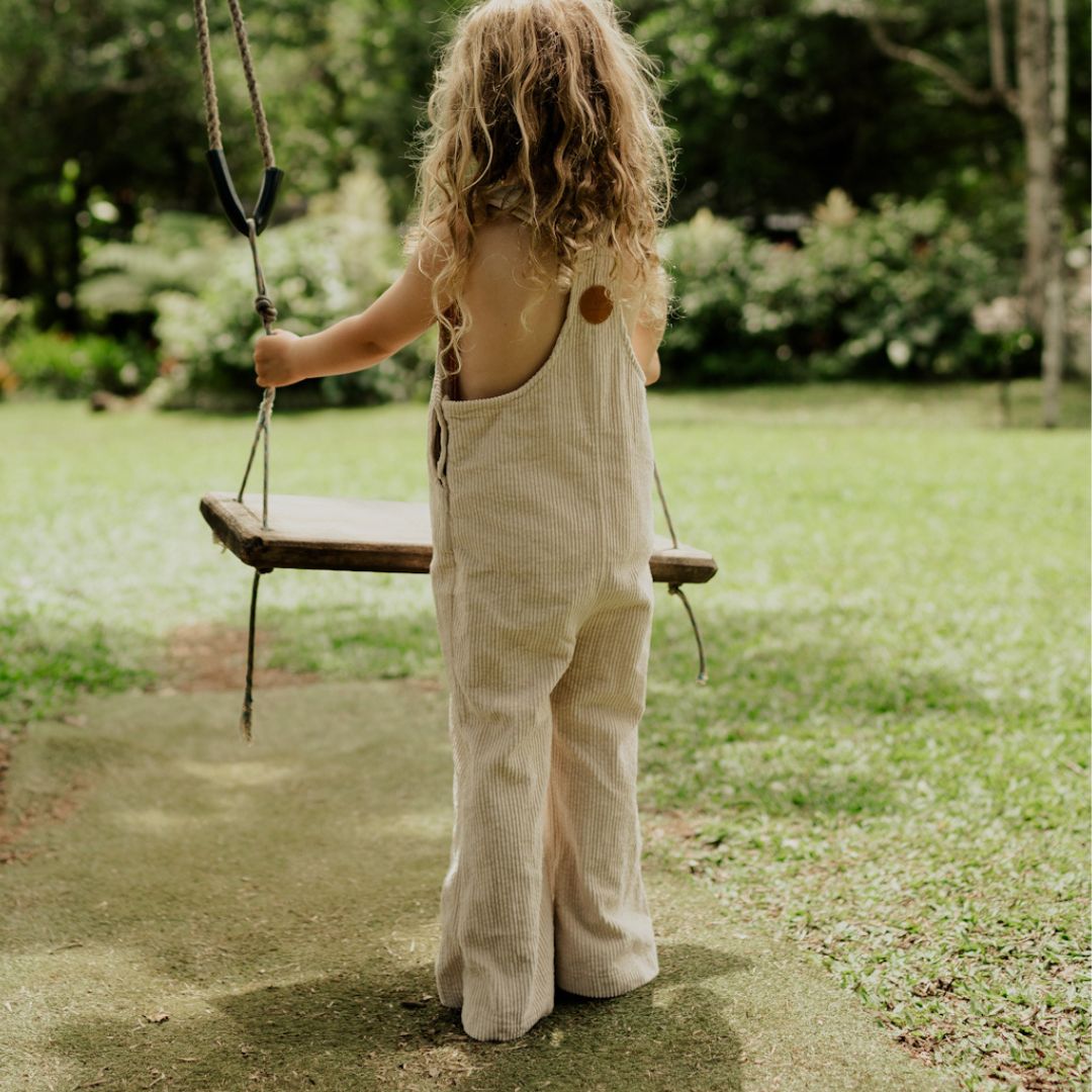 girl about to hop on a swing in nature wearing her begie Kids and toddlers corduroy flare overalls or dungarees