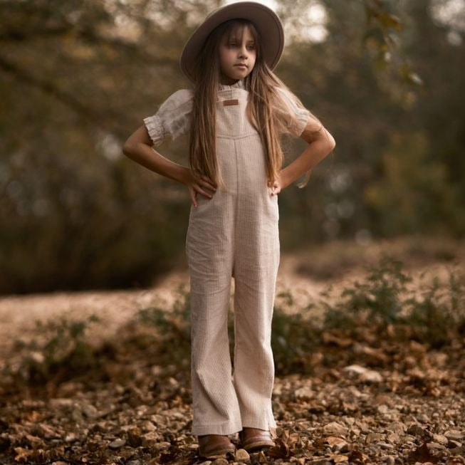 girl in nature wearing her begie Kids and toddlers corduroy flare overalls or dungarees
