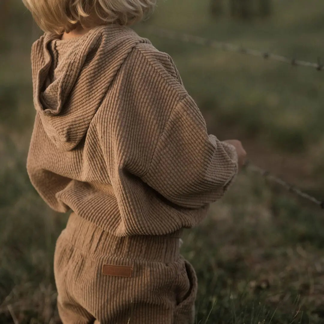 girl playing around wearing her Tan corduroy tracksuit which is has a corduroy hoodie and corduroy pants. Made from organic cotton, GOTS certified and sustainably made. back view 