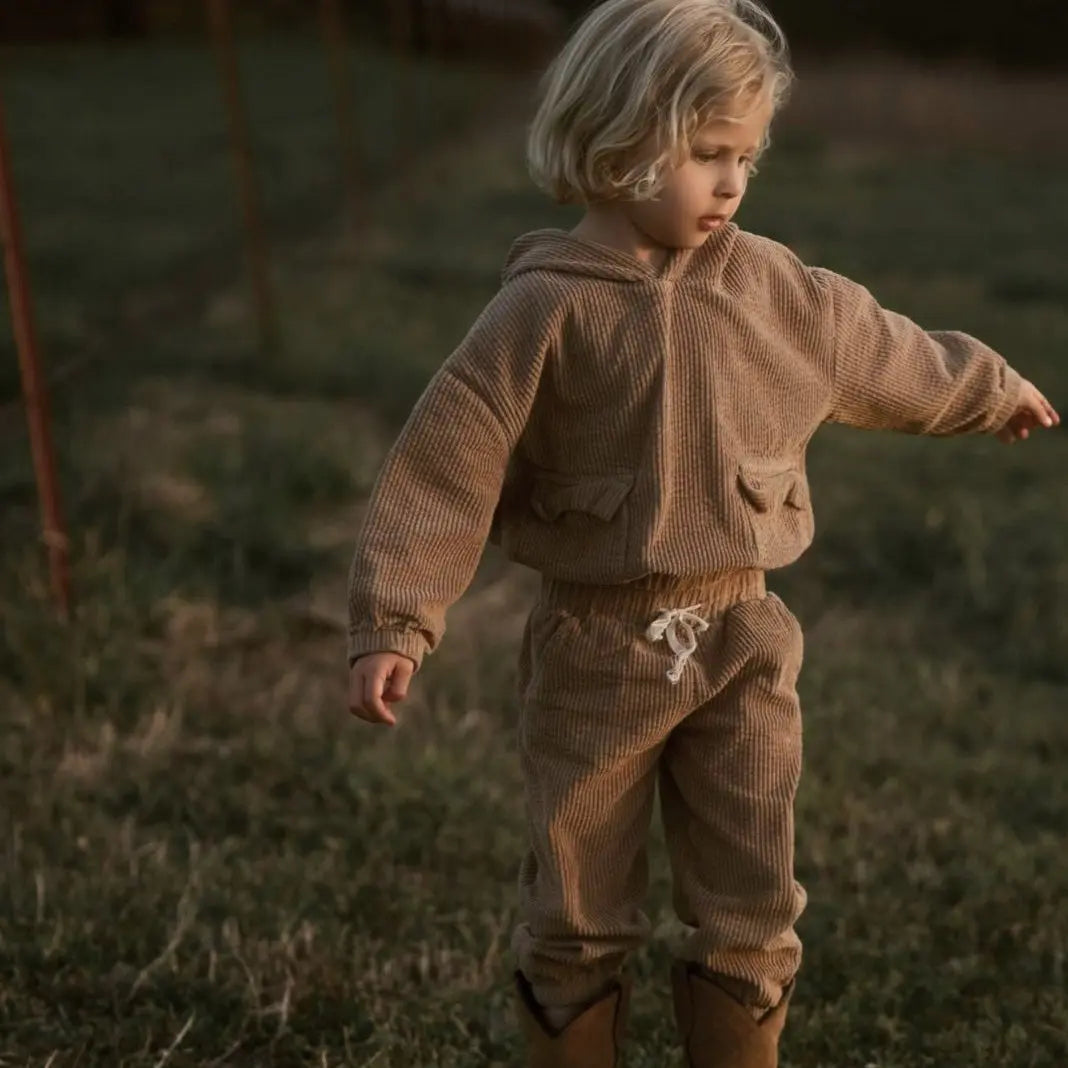 girl playing around wearing her Tan corduroy tracksuit which is has a corduroy hoodie and corduroy pants. Made from organic cotton, GOTS certified and sustainably made. front view