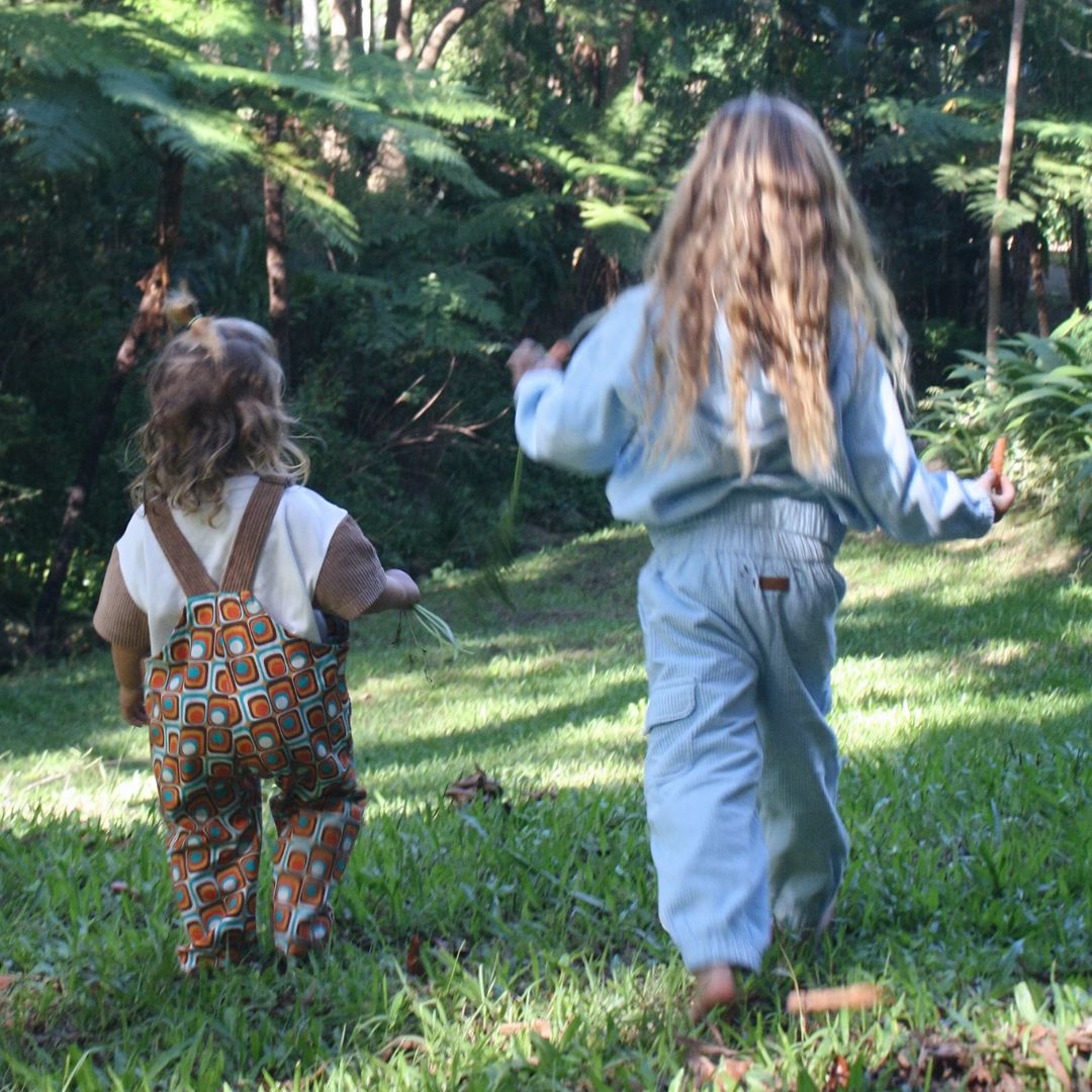 girl playing around wearing her blue corduroy tracksuit which is has a corduroy hoodie and corduroy pants. Made from organic cotton, GOTS certified and sustainably made. back view