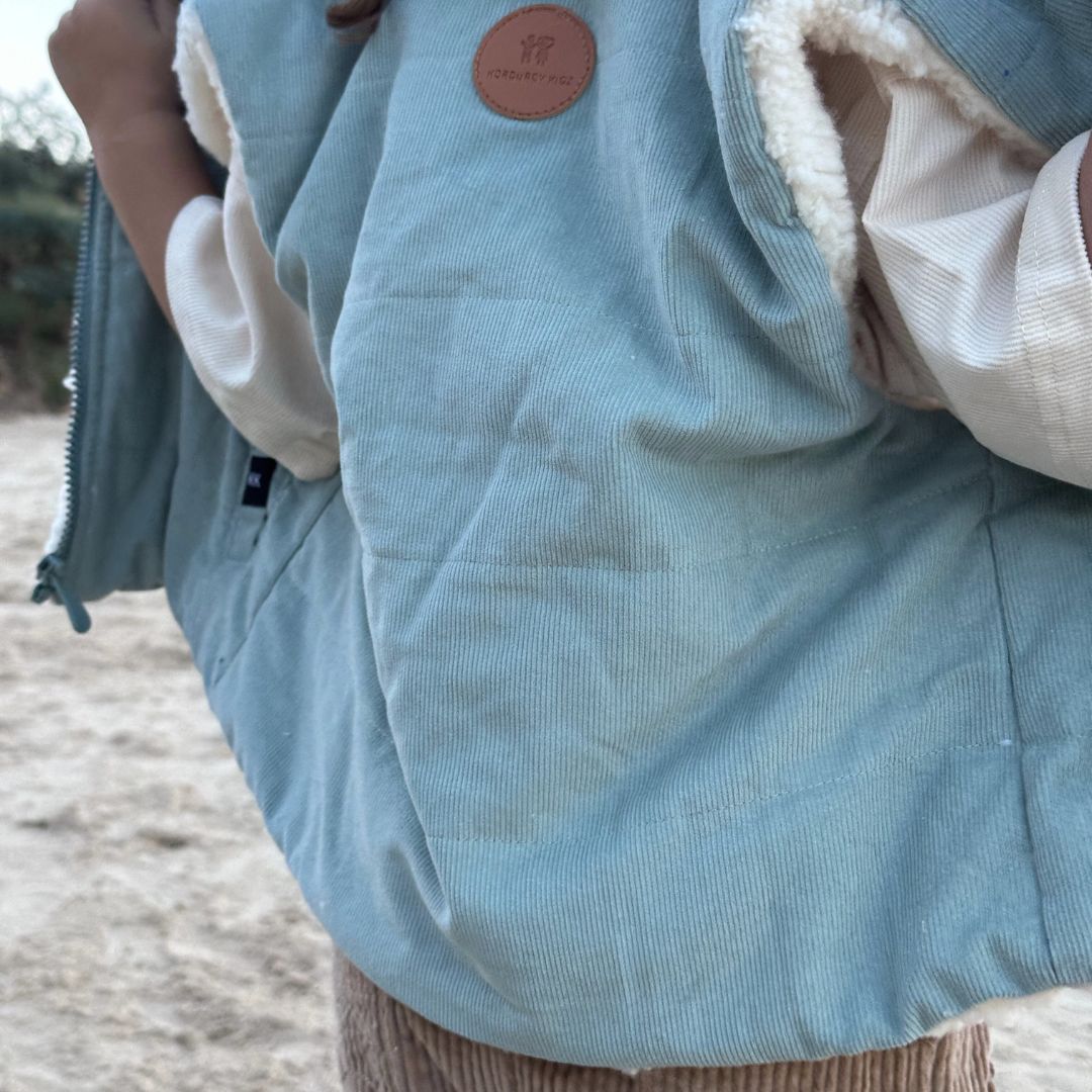 young boy wearing Kids and toddlers ocean blue colour corduroy puffer vest with back to camera taking it off