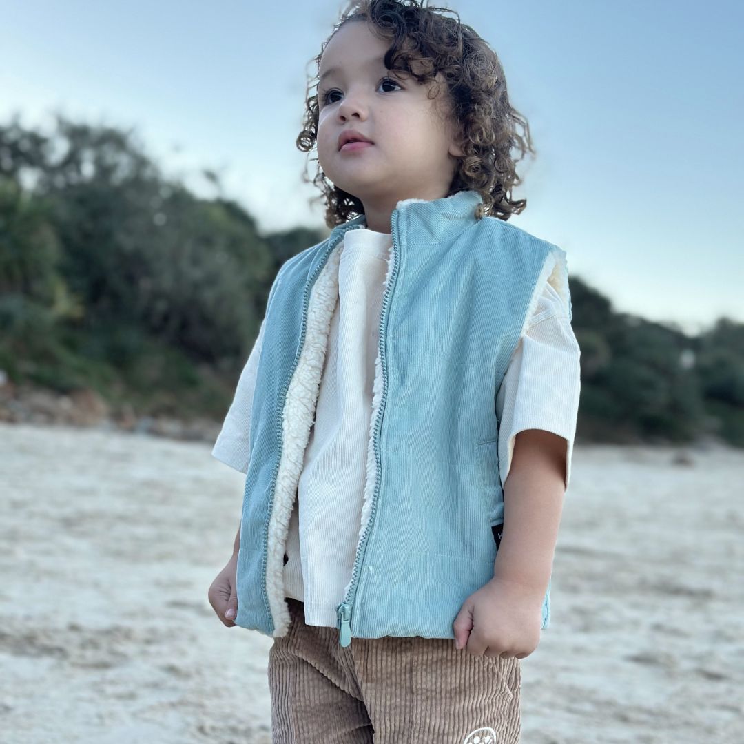 Kids and toddlers corduroy puffer vest lined with sherpa fleece facing the camera. He also has is beige corduroy t-shirt and tan corduroy shorts on