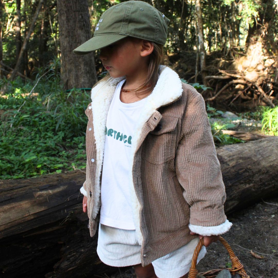 young girl wearing a kids organic corduroy sherpa fleece jacket in tan from a side angle holding a basket in nature