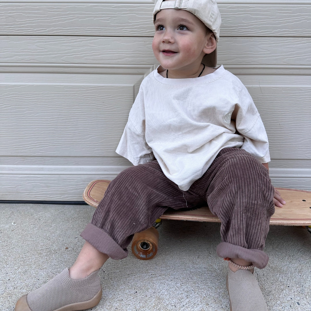 organic cotton corduroy pants in colour brown for infants, toddlers and kids sitting on skateboard