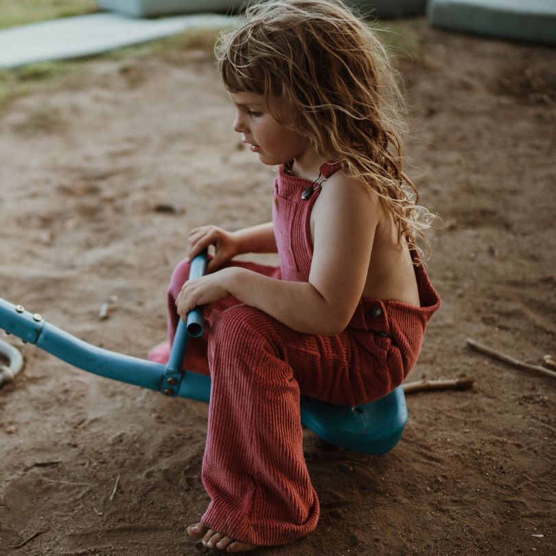 girl wearing her pink Kids and toddlers corduroy flare overalls or dungarees sitting on a seesaw