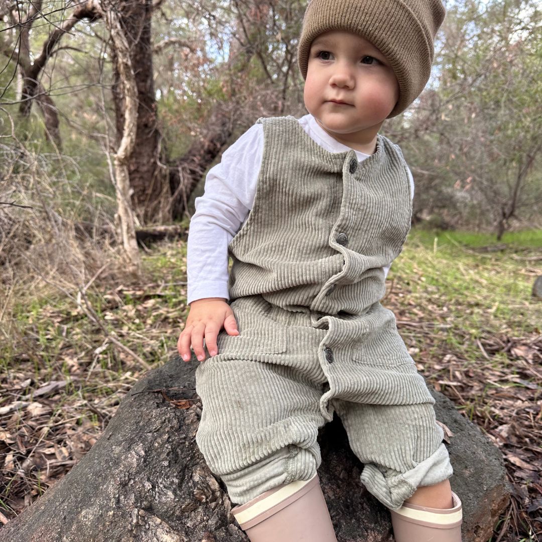 baby wearing his sage colour baby corduroy romper sitting on a rock in nature